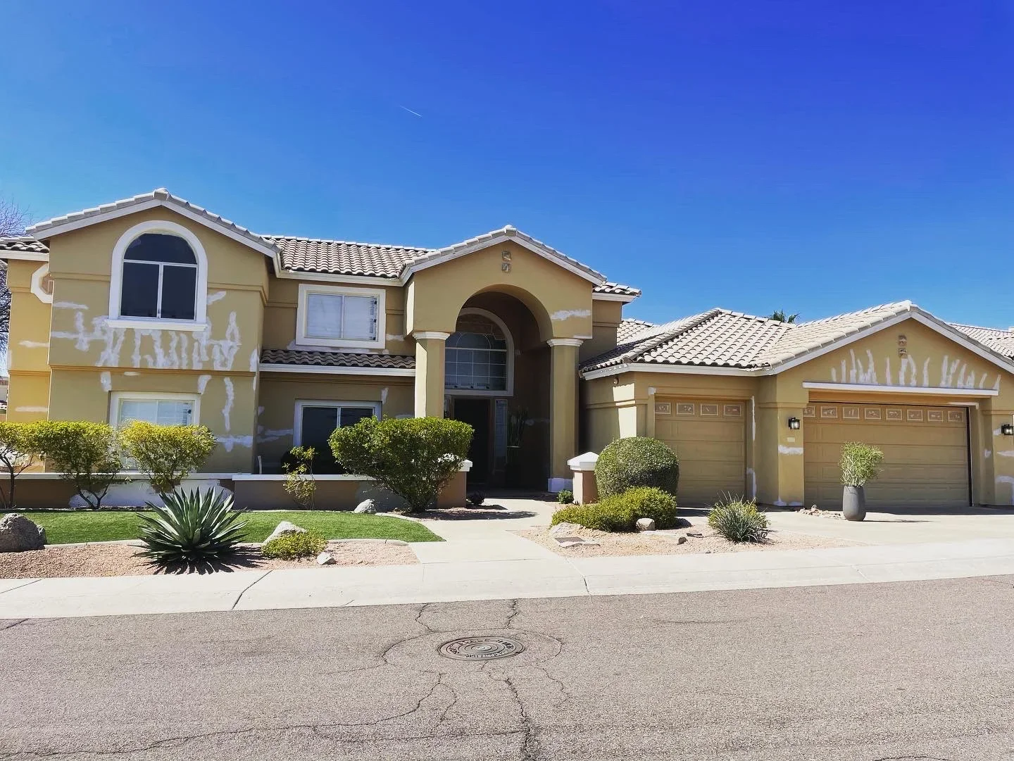 Before: Two-story stucco home showing white patch repairs before exterior repainting