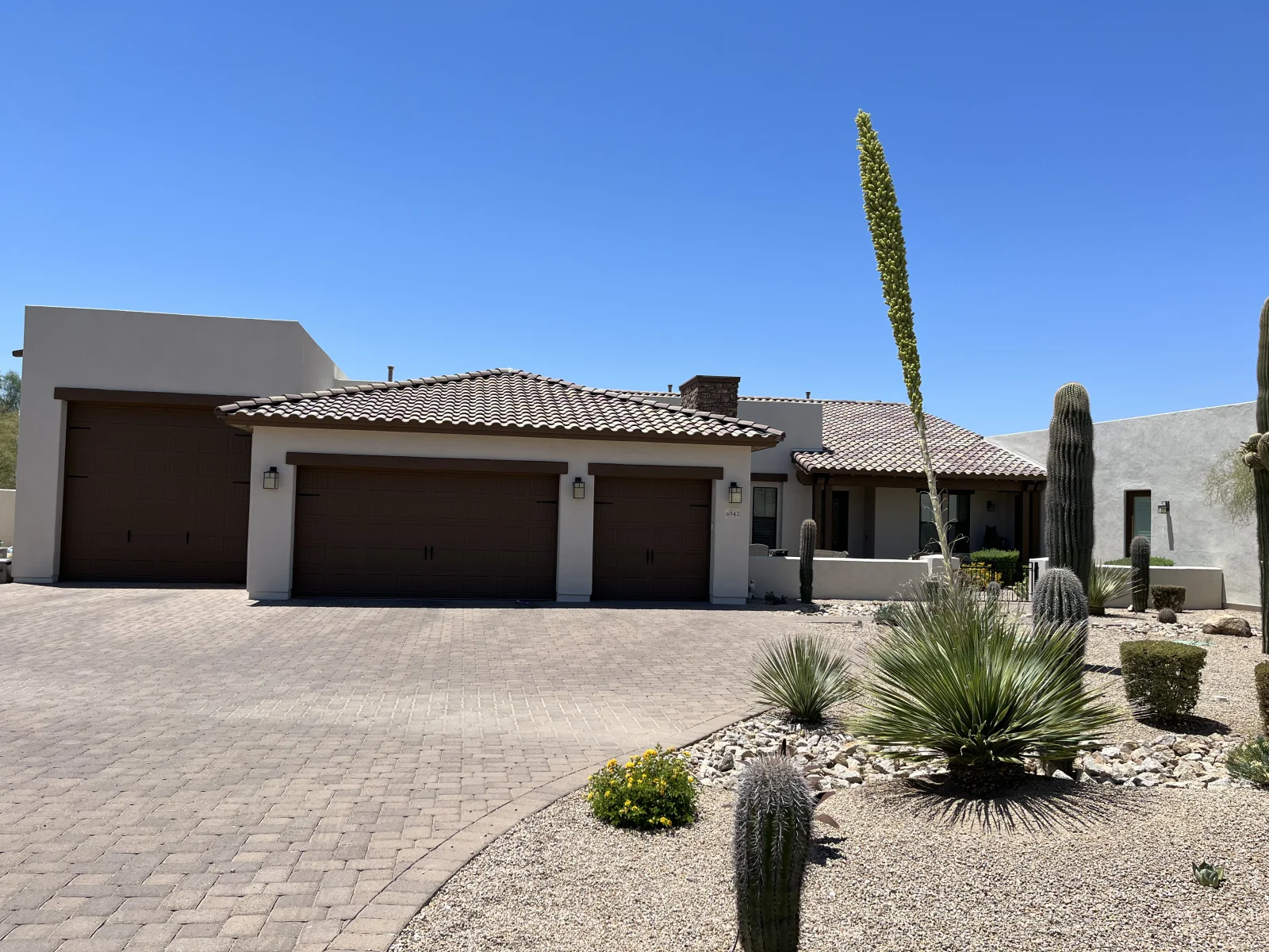 After: Smooth beige stucco home with brown garage doors and terra-cotta tile roof after exterior painting