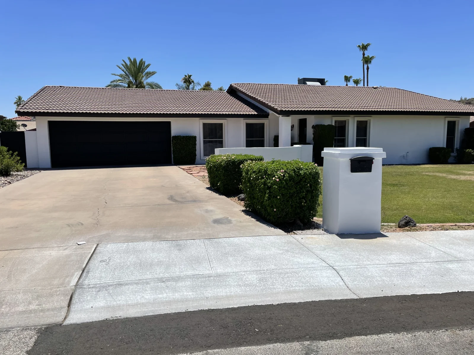 Single-story stucco home with fresh white paint, black garage door, and black roof trim after exterior painting