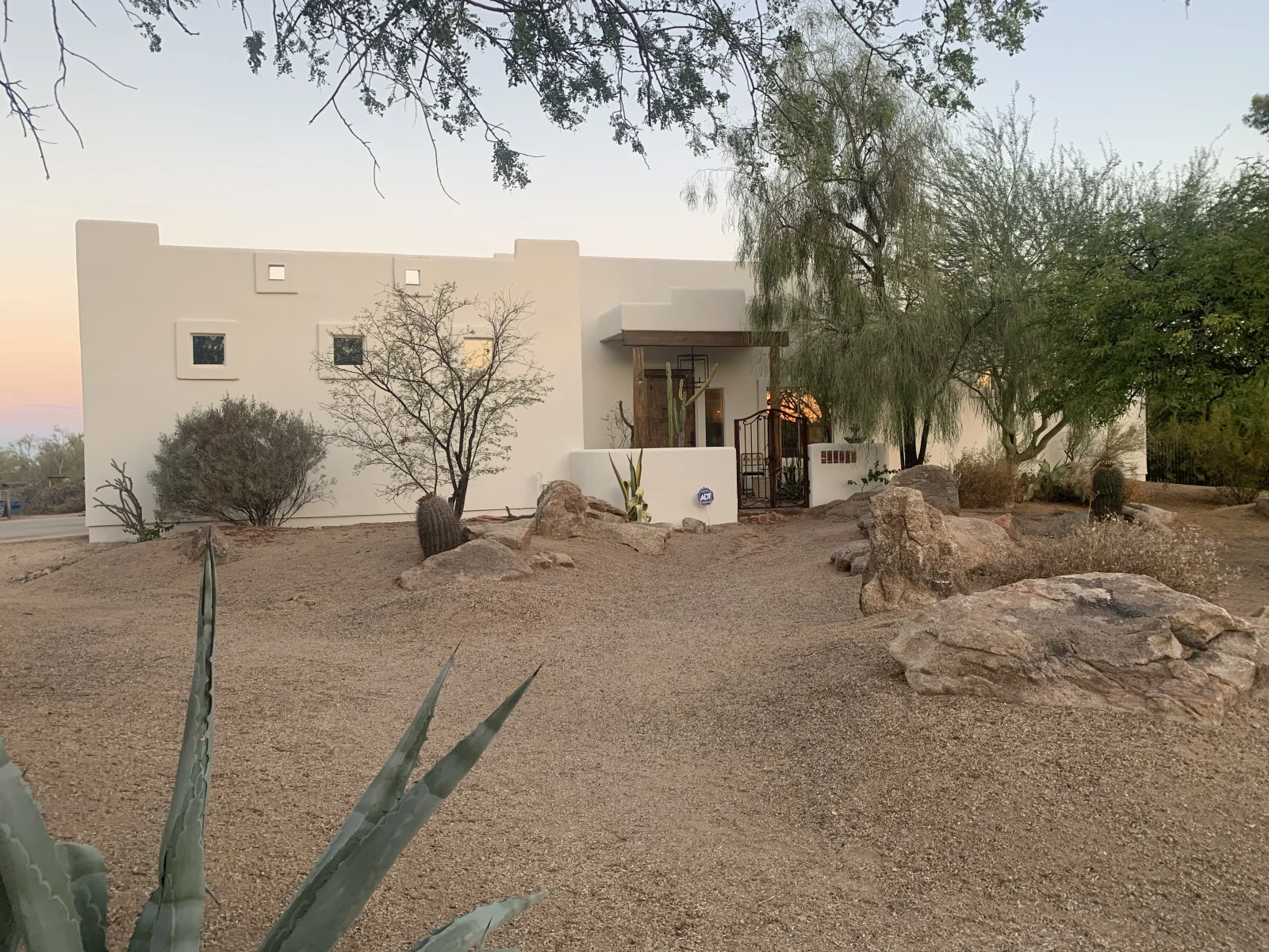 Smooth off-white stucco exterior with recessed windows, wood-beam entry portico, and wrought-iron gate after exterior painting