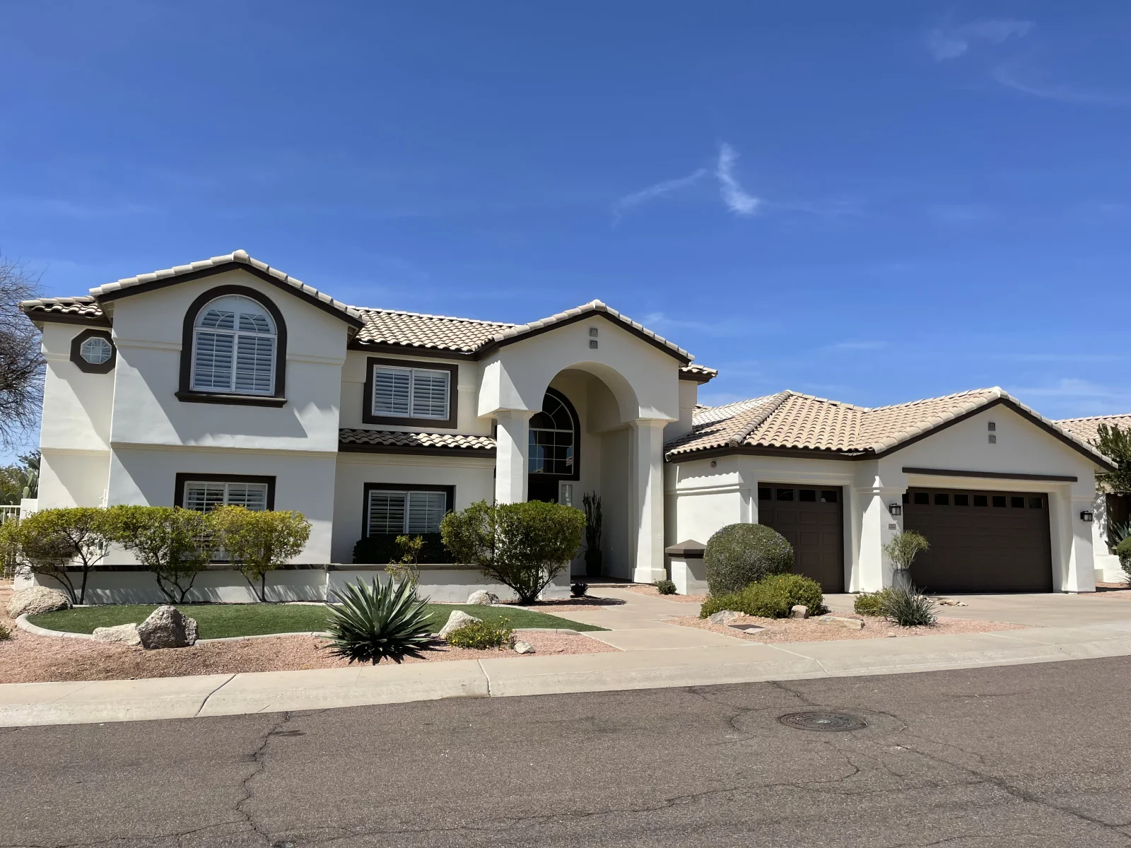 After: Two-story cream stucco home with dark brown trim and arched windows after exterior painting