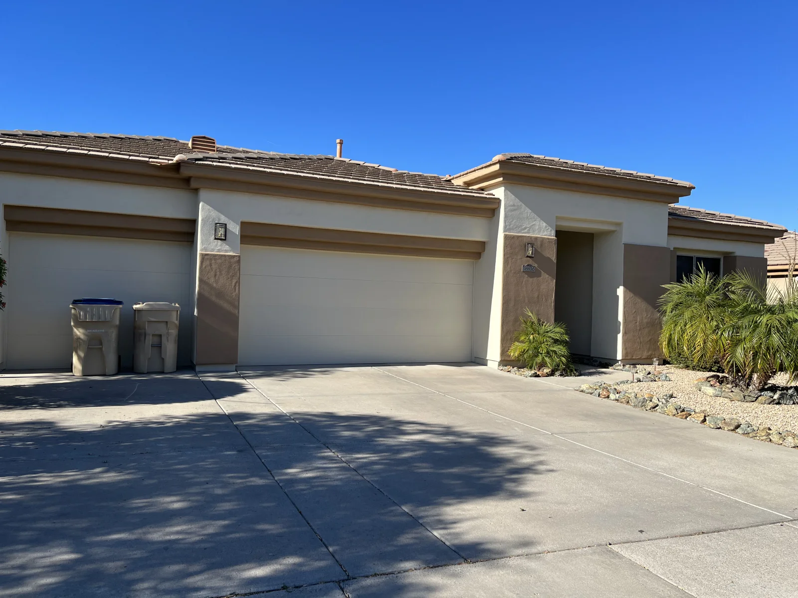 After: Single-story stucco home with cream walls and tan-brown accent trim after exterior painting