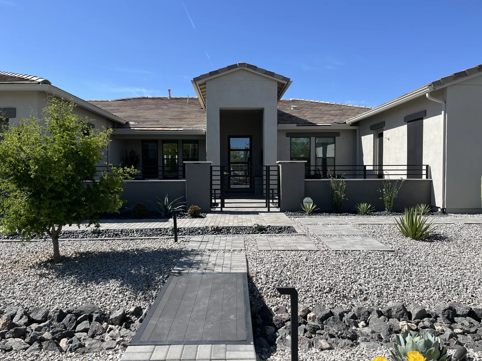Gray stucco single-story home with black metal gate, railings, and window frames after exterior painting